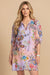 Woman wearing a colorful floral and paisley printed shift dress with tassel tie v-neck and puff sleeves from Johnny Was