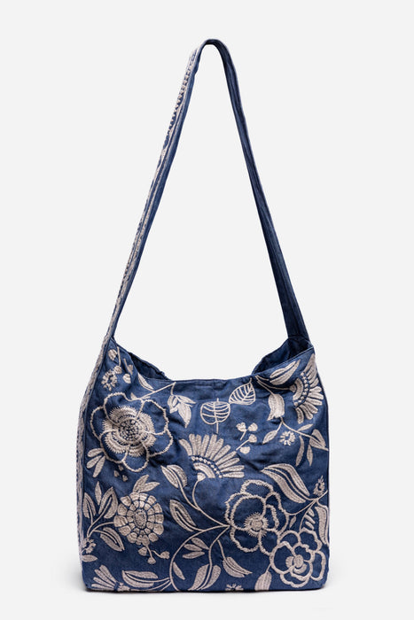 A navy blue shoulder bag with a white floral and botanical pattern, featuring a single shoulder strap and a structured, soft slouchy silhouette, shown against a plain light gray background.