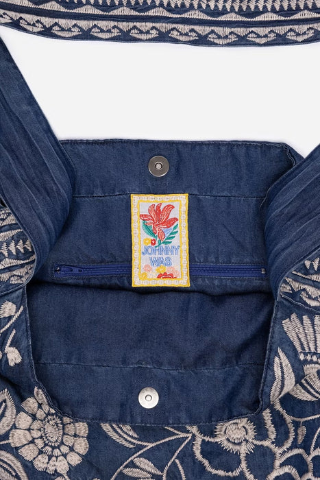 Close-up of a dark blue denim garment with cream floral embroidery and a central embroidered patch reading 'Johnny Was'.