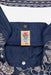 Close-up of a dark blue denim garment with cream floral embroidery and a central embroidered patch reading 'Johnny Was'.