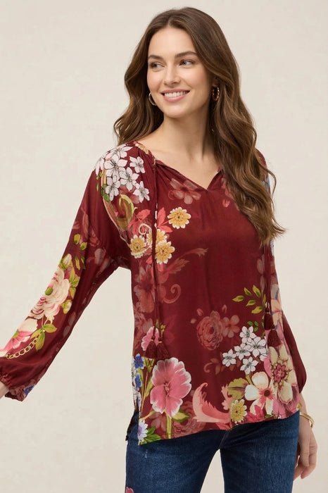 Woman wearing a red floral printed blouse with split v-neck tassel tie from Johnny Was