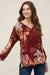 Woman wearing a red floral printed blouse with split v-neck tassel tie from Johnny Was