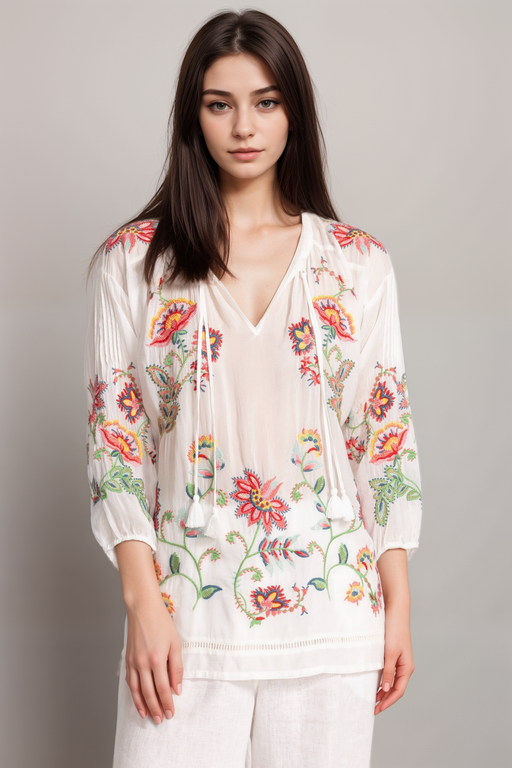 Woman wearing a white blouse with colorful floral embroidery and tassel v-neck from Johnny Was