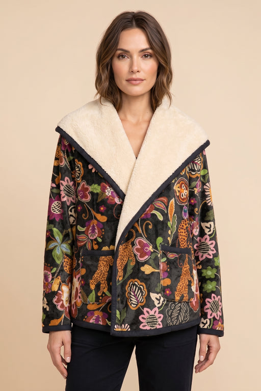 A woman wearing a black patchwork jacket with a cream-colored shearling collar and a colorful floral and animal print, set against a solid beige background.