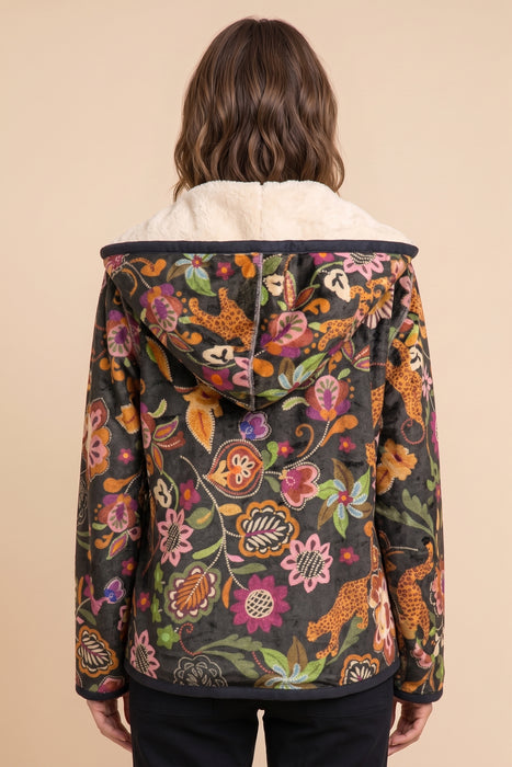 A woman viewed from the back wearing a hooded jacket with a dark base covered in a dense multicolor floral and animal print, with a cream sherpa collar, against a solid beige background.