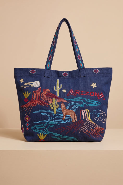 A navy blue tote bag with colorful embroidered desert and Arizona-themed designs, including a cactus, horse, moon, stars, and the word 'ARIZONA' in red, shown against a beige background.