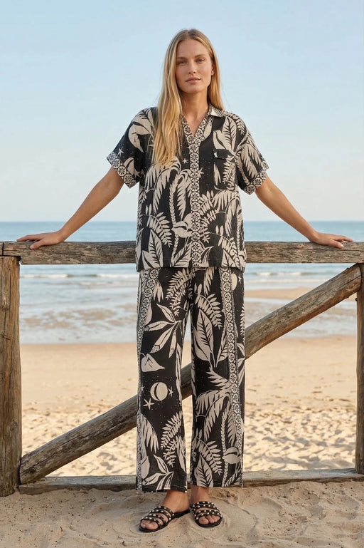 Woman wearing a black and white tropical patterned button down shirt with short sleeves and chest pocket from Johnny Was