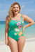 Woman wearing a floral green one piece swimsuit on a beach from Johnny Was