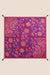 A square scarf with a vibrant purple background and an intricate paisley and floral pattern in orange, red, and pink, finished with small tassel corners, shown flat against a light beige background.