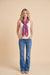 A woman modeling a vibrant purple and pink patterned silk scarf tied around her neck, paired with a white sleeveless top and blue jeans, against a solid beige studio background.