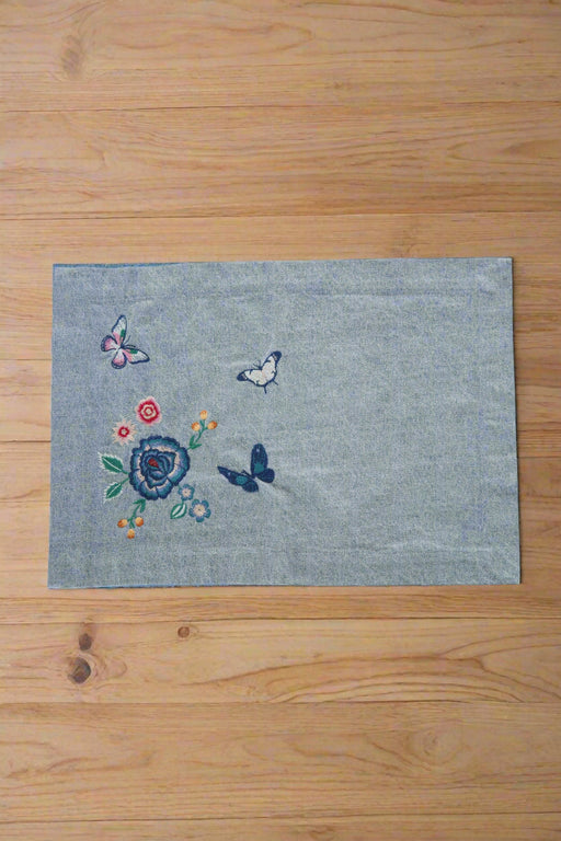 A blue , rectangle, denim placemat with floral and butterfly embroideries