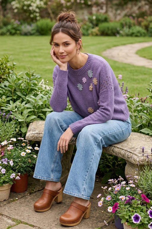 Woman wearing a purple pullover sweater with colorful flower appliqués and open knit detail from Johnny Was