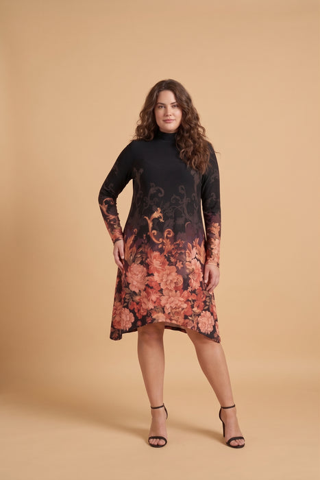 A woman modeling a long-sleeve mock-neck midi dress with a black base and a large floral print in warm coral, orange, and pink tones that fade into a darker pattern near the hem, set against a solid beige studio background.