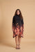 A woman modeling a long-sleeve mock-neck dress with a black upper section and a floral gradient pattern in shades of orange, pink, and red on a black base, set against a solid beige studio background.