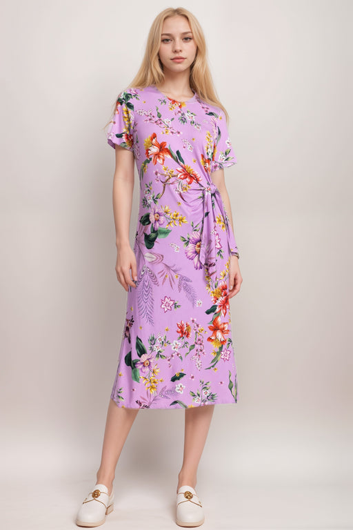 Woman wearing a purple midi dress with colorful florals and side tie detail from Johnny Was