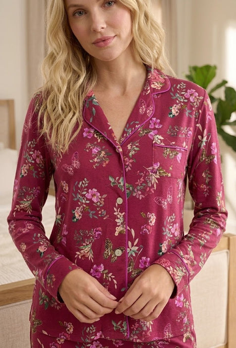 A woman wearing a long-sleeve button-front pajama top in dusty rose pink with a floral print, shown in a softly lit indoor setting.