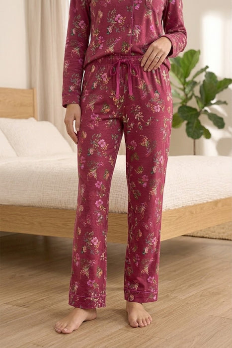 A person wearing a matching long-sleeve pajama top and pants set in dusty rose pink with a floral print, standing barefoot in a bedroom setting.