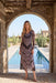 A woman stands in a stone archway with a resort pool and cacti behind her, wearing a long-sleeve midi dress with a black and dusty pink paisley pattern.