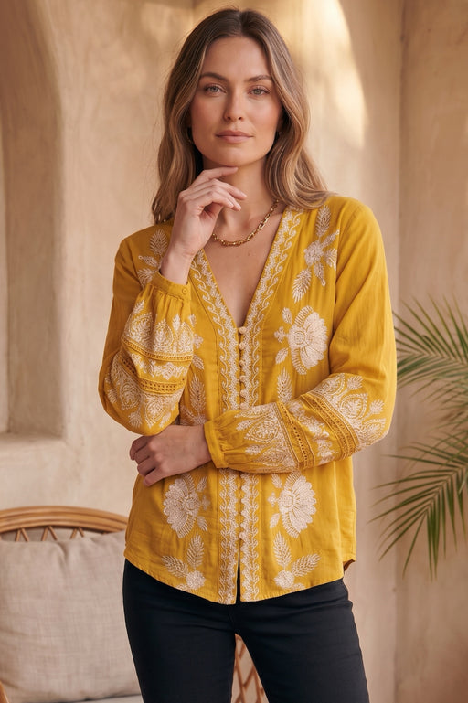 Woman wearing a yellow embroidered blouse with v-neck and button front from Johnny Was