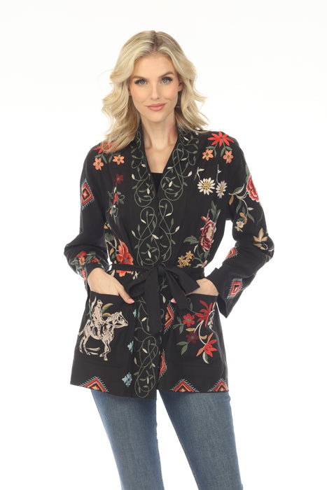 Woman wearing a black floral embroidered military style jacket with self-tie belt and side pockets from Johnny Was