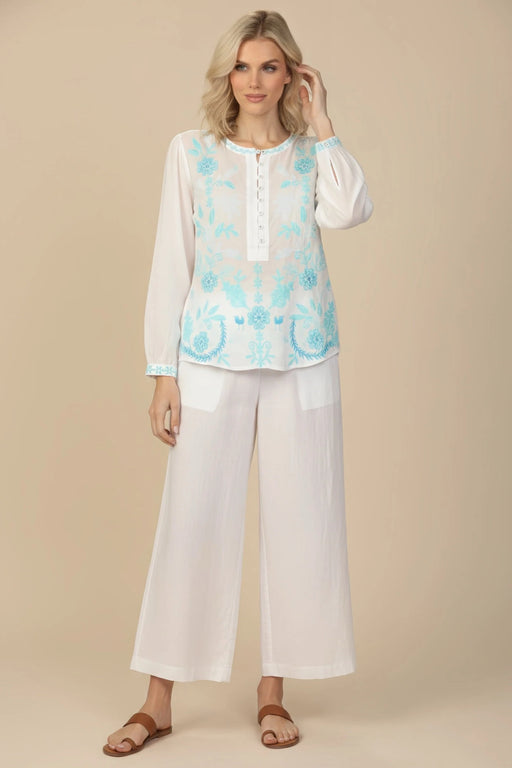 Woman wearing a white henley long sleeve blouse with blue floral embroidery from Johnny Was