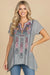 Woman wearing a gray embroidered tunic with split v-neck and short sleeves from Johnny Was