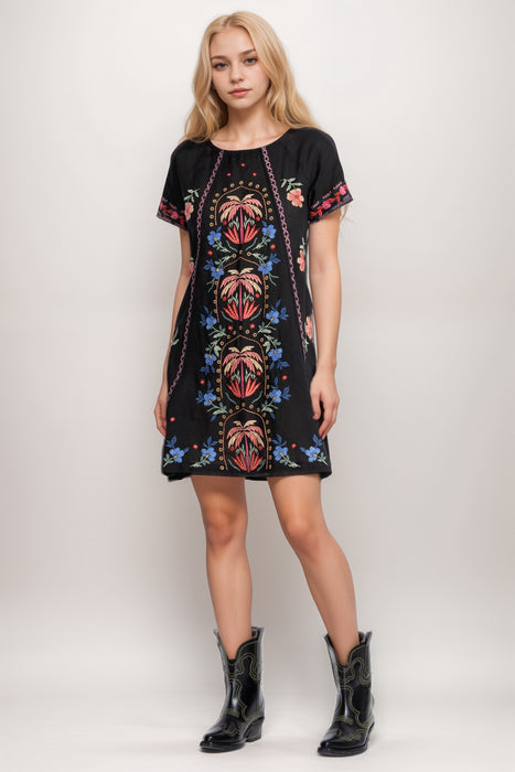 Woman wearing a black dress with colorful embroidered patterns and raglan sleeves from Johnny Was