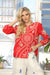 Woman wearing a red embroidered blouse with intricate patterns and button front from Johnny Was