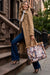 A woman stands on brownstone steps holding a large floral tote bag from Johnny Was
