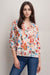 Woman wearing a silk blouse with colorful floral print, pintuck, and ruffle detail on the 3/4 sleeves