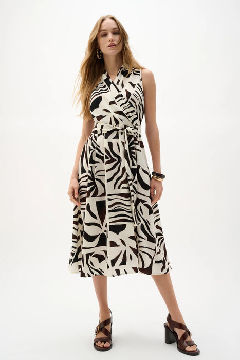 Woman wearing Joseph Ribkoff beige multi tropical print fit and flare wrap dress, featuring a sleeveless design, tie waist, lightweight gauze fabric, and a flowy feminine silhouette.