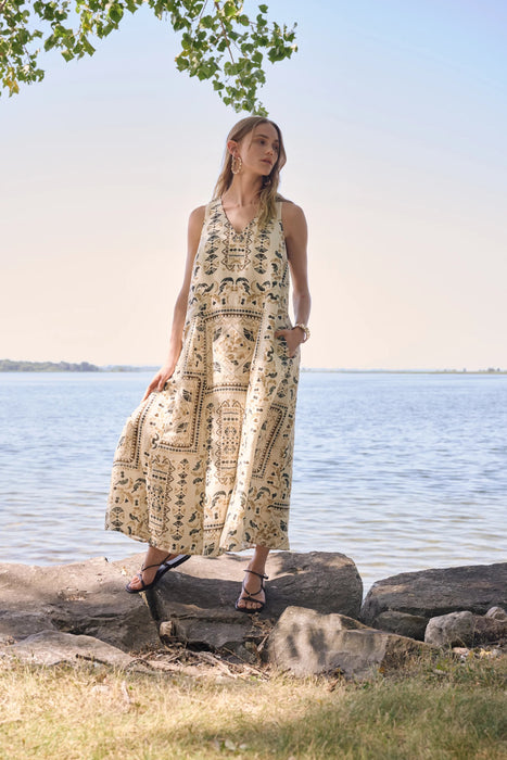 Woman wearing a scarf print linen blend A-line dress standing by a lakeside in a breezy summer setting.