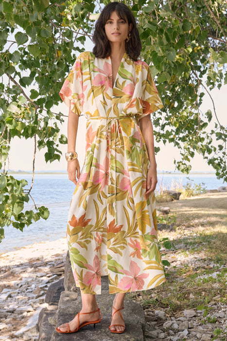 Woman wearing a beige multi tropical print fit and flare dress with tie waist, styled outdoors by the water for a chic summer look