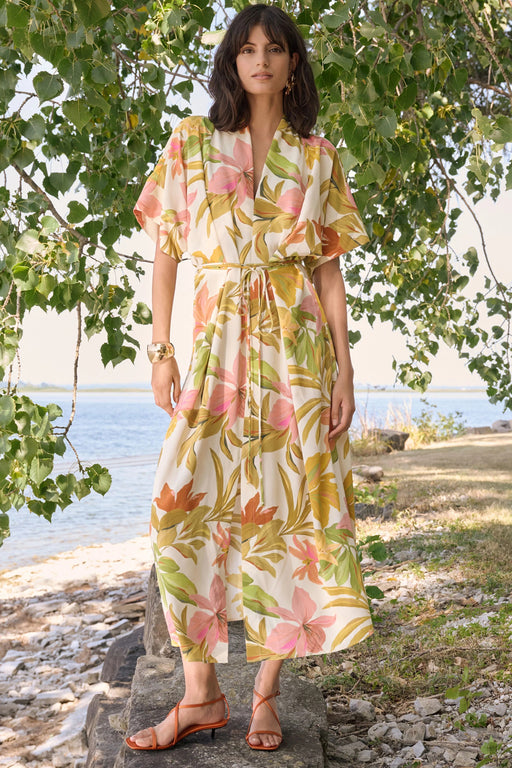 Woman wearing a beige multi tropical print fit and flare dress with tie waist, styled outdoors by the water for a chic summer look
