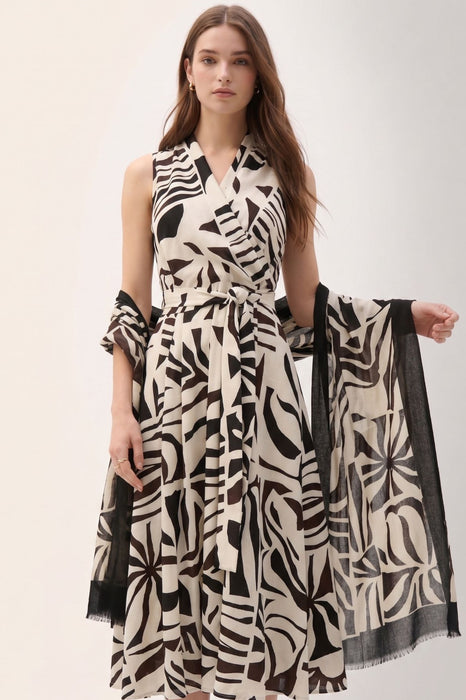 Woman wearing a two-tone scarf in beige and black with tropical print and fringe edges from Joseph Ribkoff