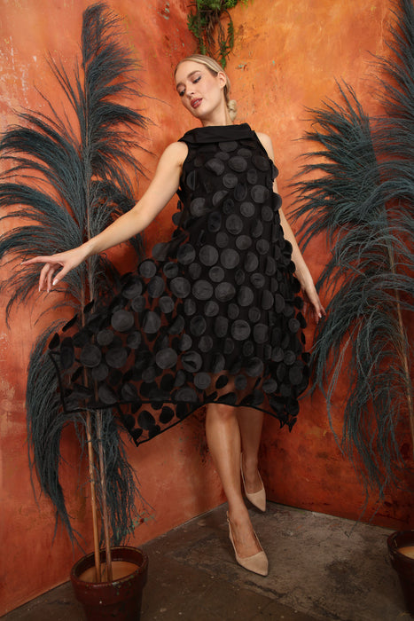 Woman wearing a black trapeze mesh dress with 3D polka dots and cowl neckline