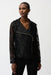 Woman wearing a black sheer textured moto jacket with asymmetric zipper and structured lapel collar, styled with black pants.