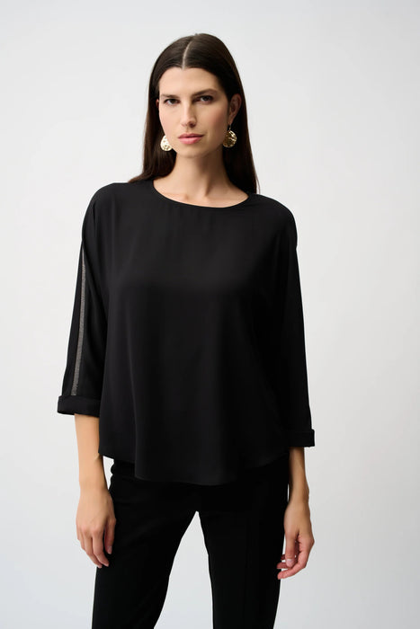 Woman wearing a black lightweight blouse with contrasting rhinestone embellishments on the 3/4 sleeves
