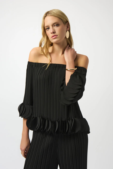 Woman wearing a black lightweight pleated top with off-shoulder and circle appliqué detail at the sleeves and hem