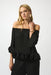 Woman wearing a black lightweight pleated top with off-shoulder and circle appliqué detail at the sleeves and hem