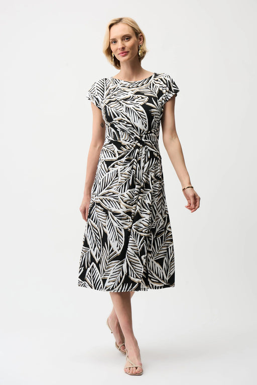 Model wearing Joseph Ribkoff black multi tropical print silky knit fit and flare dress with waist tie and short sleeves for a flattering feminine silhouette.