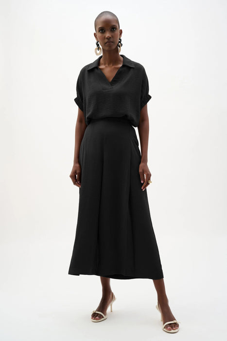 Woman wearing a black Joseph Ribkoff pull-on culotte pants with pleats, featuring flowy wide-leg silhouette, cropped length, and a flattering high-rise modern fit.