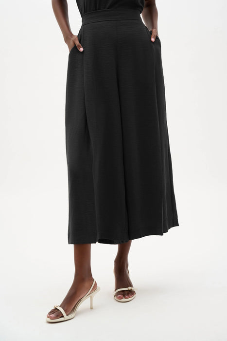 Woman wearing a black Joseph Ribkoff pull-on culotte pants with pleats, featuring flowy wide-leg silhouette, cropped length, and a flattering high-rise modern fit.