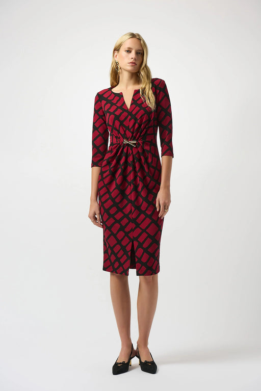 Woman wearing a red and black geometric patterned dress with a ruched waist and ornament from Joseph Ribkoff