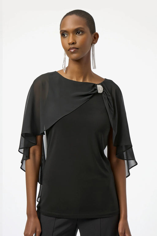 Woman wearing a black top with sheer chiffon cape overlay and rhinestone brooch