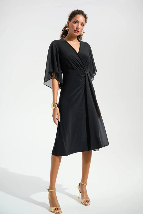 Woman wearing a black knee-length dress with surplice neck and flutter chiffon sleeves from Joseph Ribkoff