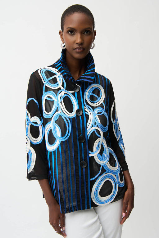 Woman wearing a black multi abstract print jacket with bell sleeves and button front, styled with white pants.