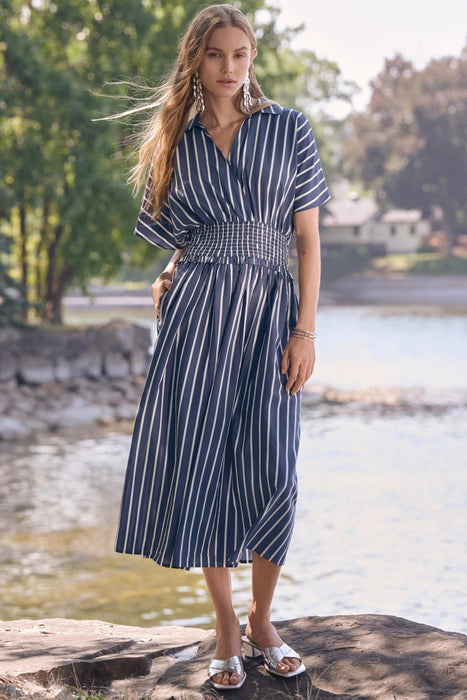 Woman wearing a blue midi fit and flare dress with white stripes and smocked waist from Joseph Ribkoff
