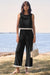 Woman wearing a black and white contrast trim culotte jumpsuit with wide-leg silhouette by the water, styled with sandals and a woven handbag.