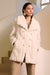 Woman wearing a cream colored faux fur coat with double breast design and shawl collar from Joseph Ribkoff